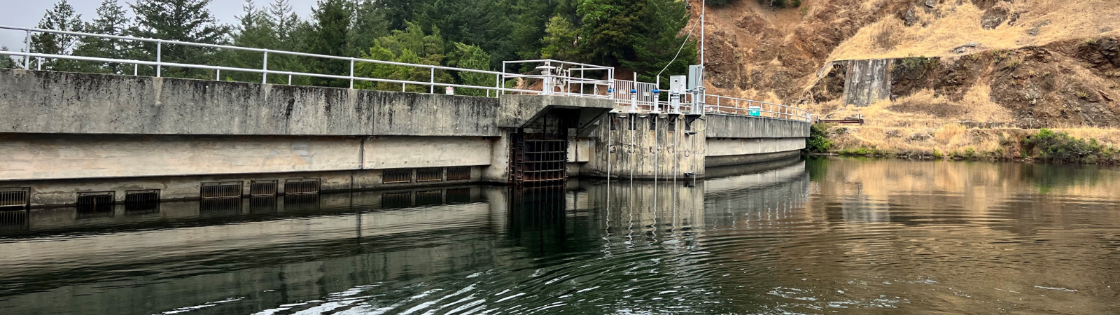 A concrete arch dam is reflected in the smooth surface of a reservoir. 