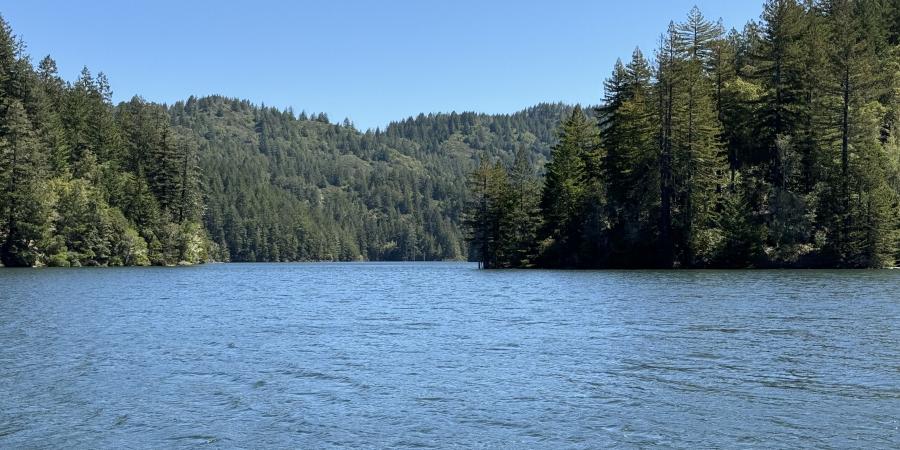 Reservoir with forested hills and a clear sky.