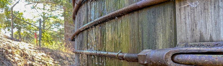 Water drips past metal belts wrapped around redwood slats as part of a massive water storage tank.