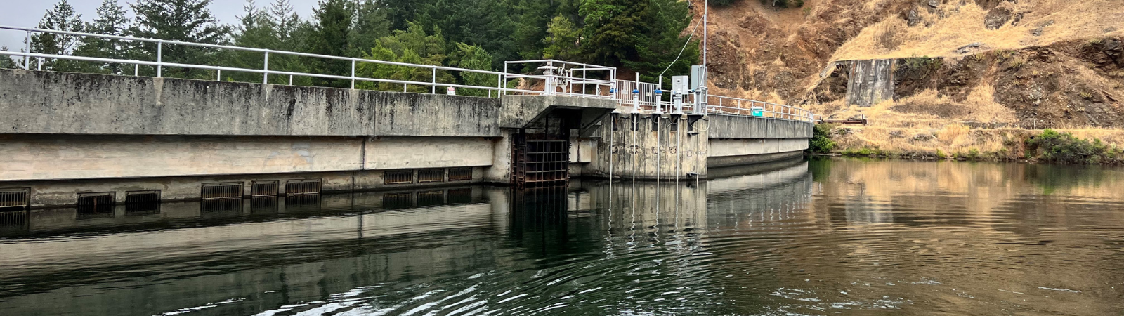 A concrete arch dam is reflected in the smooth surface of a reservoir.