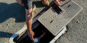 A person points toward a water meter in the ground.